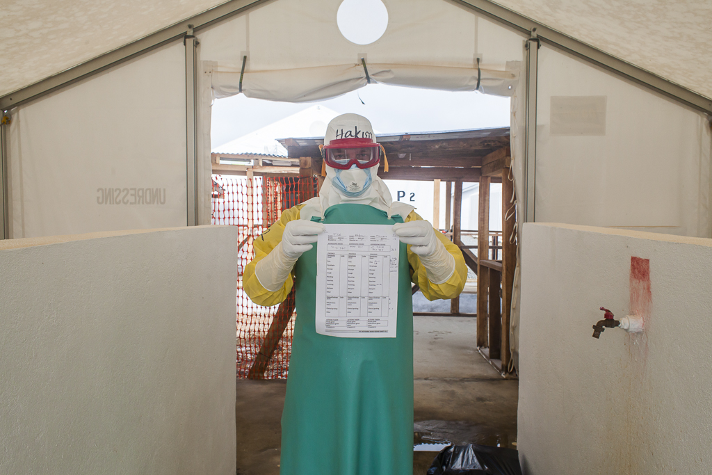 Hakon, the Norwegian doctor in charge of the medical team, standing in the border line of the high risk contagion area with medium risk area. He is showing a list of symptoms of a patient, this paper is always photographed by a nurse, so the medical office can get all the information. The reason is that no one item can be carried back from the high risk zone (triage, ambulances bay, patient´s area and morgue) without a long soaking in chlorine solution. In general, with the exception of some of the Ebola protective clothing items, all the things which enter in the high risk area are burnt inside it. Ebola Treatment Center. Moyamba. Sierra Leone.
